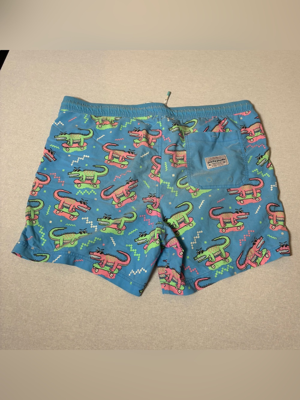 blue Party Pants swim trunks with an all-over neon alligator